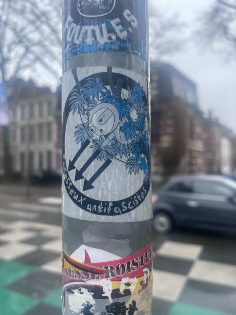 Photo d'un poteau avec collé dessus un sticker du collectif Jeune Garde Lille accompagné de l'écriteau "Paresseux antifasciste" ©Raphaël Pazuelo